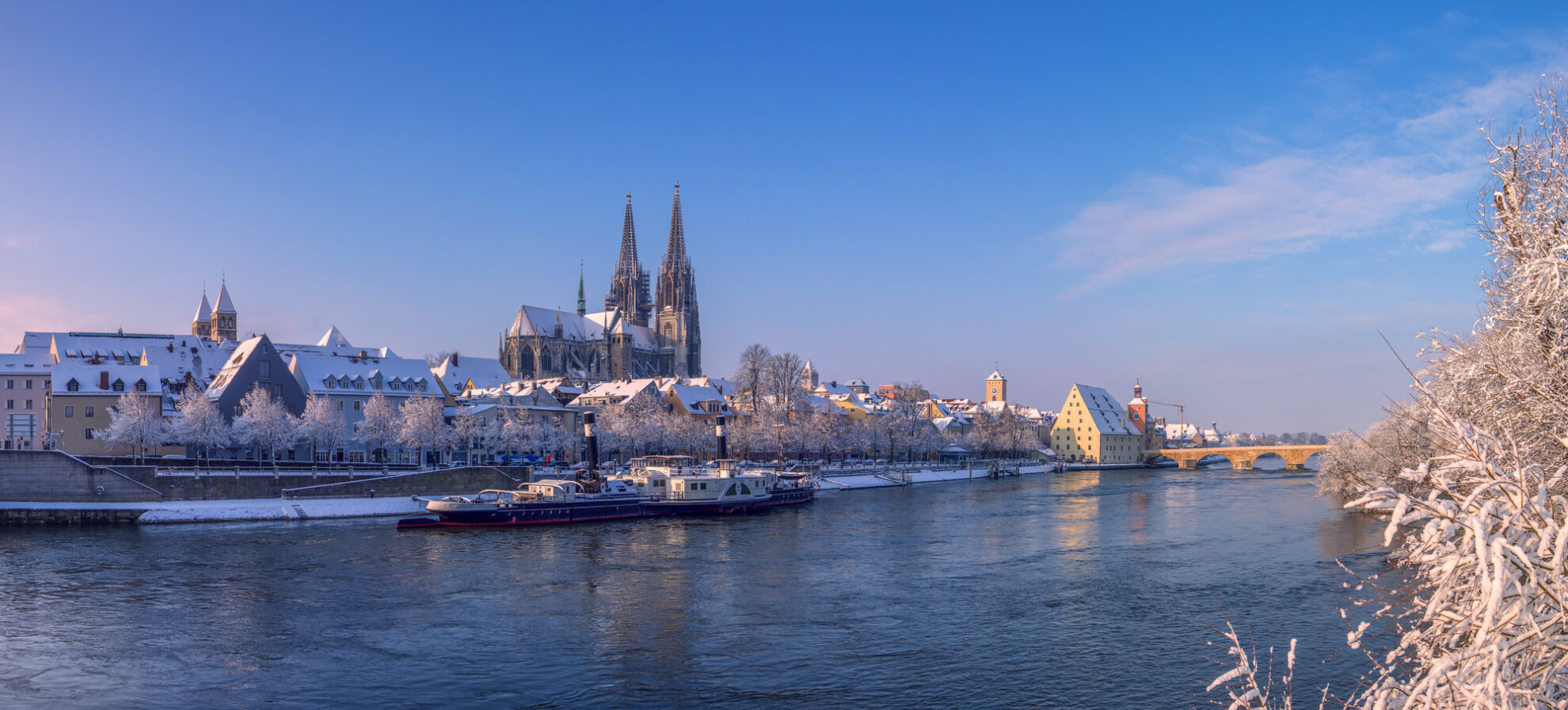 Winterpanorama von Regensburg – verschneite Altstadt mit Dom, Steinerner Brücke und Donauufer.