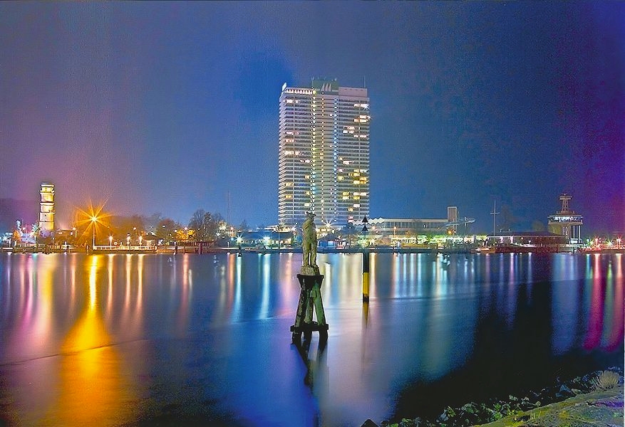 Blick auf die beleuchtete Skyline von Travemünde mit dem Maritim-Hochhaus am Hafen – ein beliebtes Ziel für Ostsee-Urlaub und Busreisen nach Lübeck-Travemünde.