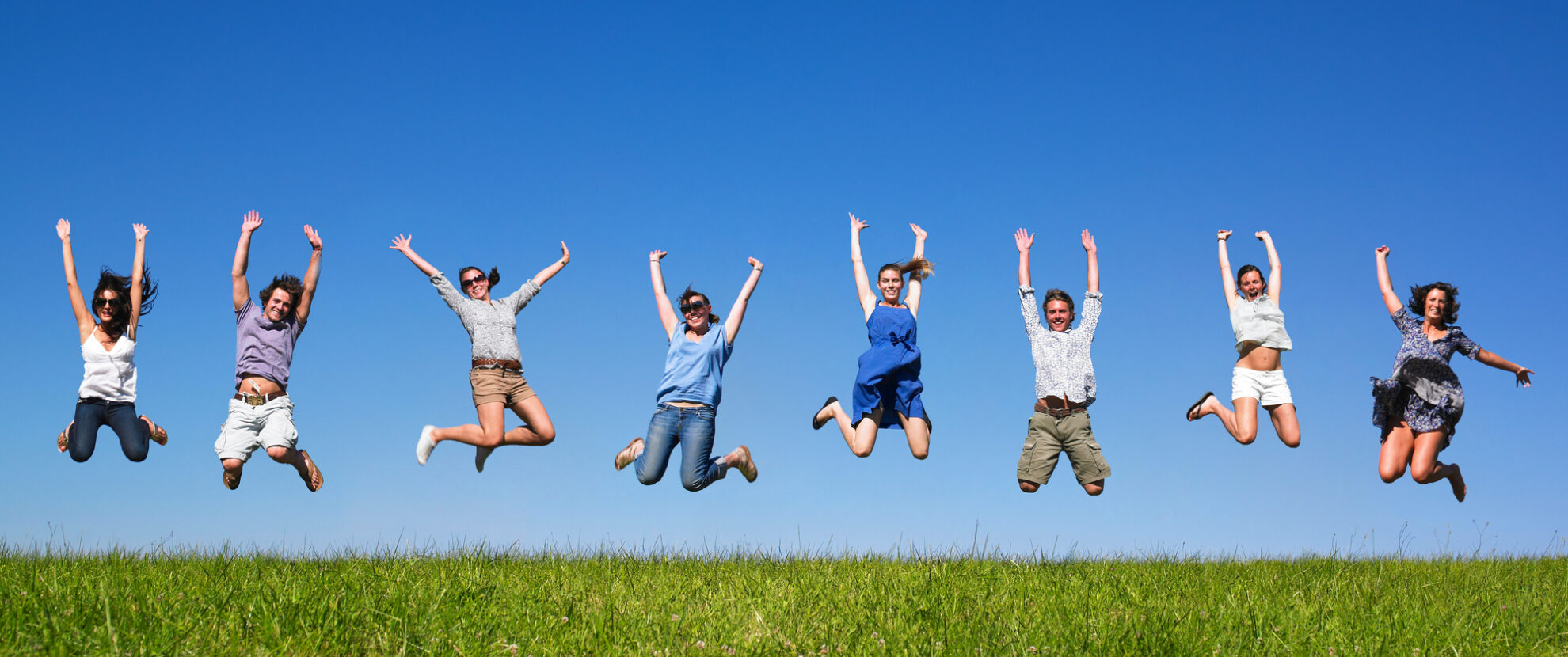 Glückliche Gruppe junger Menschen springt in die Luft – Lebensfreude, Gemeinschaft und Energie unter blauem Himmel.