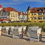 Strandkörbe am Sandstrand vor historischen Gebäuden bei sonnigem Wetter.