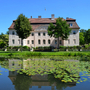 Herrenhaus mit Spiegelung in einem Teich voller Seerosen, sonniges Wetter.