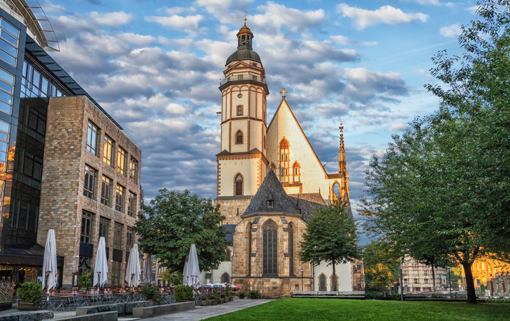 Kirche mit imposantem Turm neben modernen Gebäuden unter bewölktem Himmel.