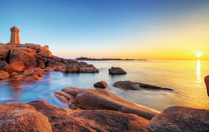 Küste mit Felsen und Turm, Sonnenuntergang über dem Meer.