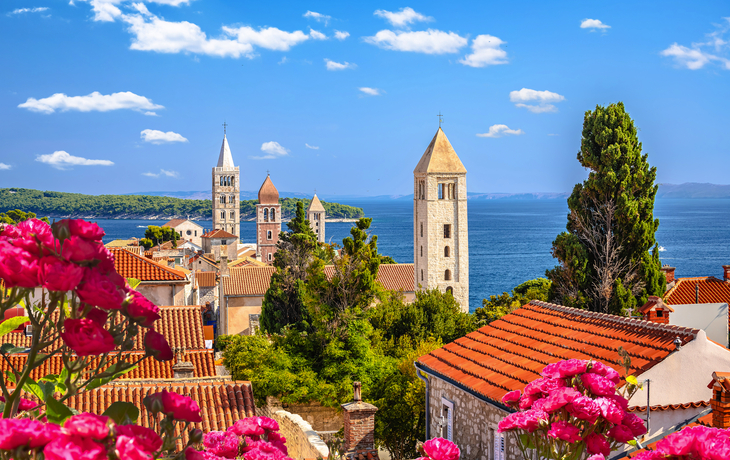 Mittelalterliche Stadt mit roten Dächern, Türme und Meer im Hintergrund.