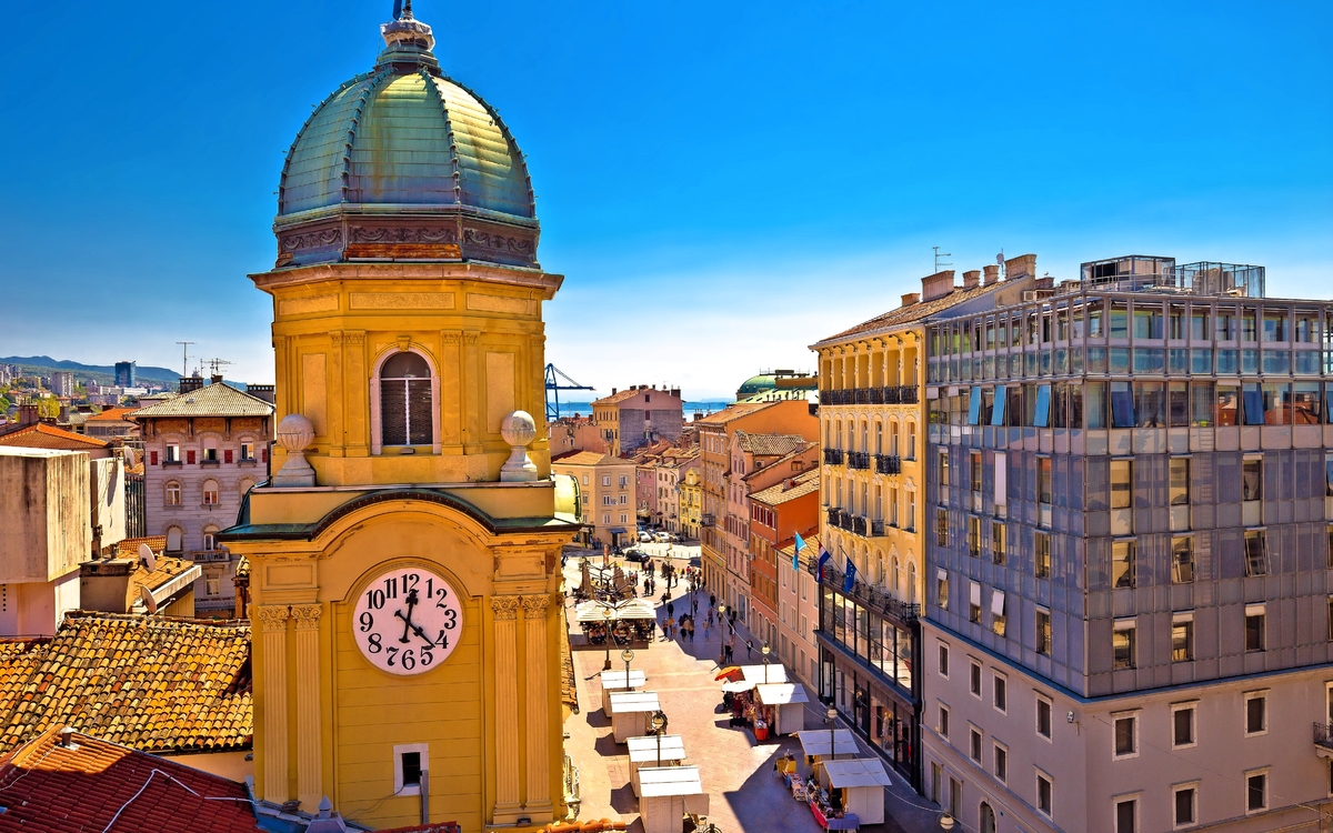 Stadtszene mit Uhrturm und historischen Gebäuden bei klarem Himmel.