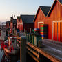 Rote Bootshäuser und Fischkutter entlang eines Holzdocks in der Abenddämmerung.
