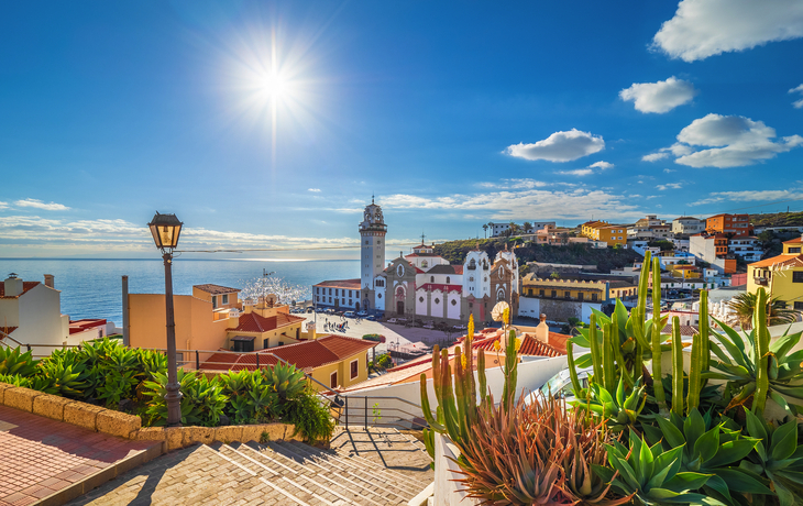 Treppen führen zu einer Kirche in einem sonnigen Küstendorf mit Blick aufs Meer.