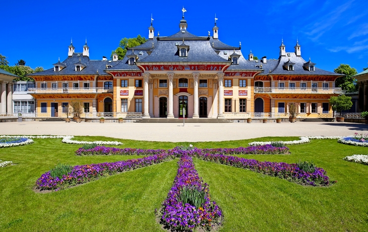 Pillnitz Barockschloss mit Garten und blühenden Blumen im Vordergrund.