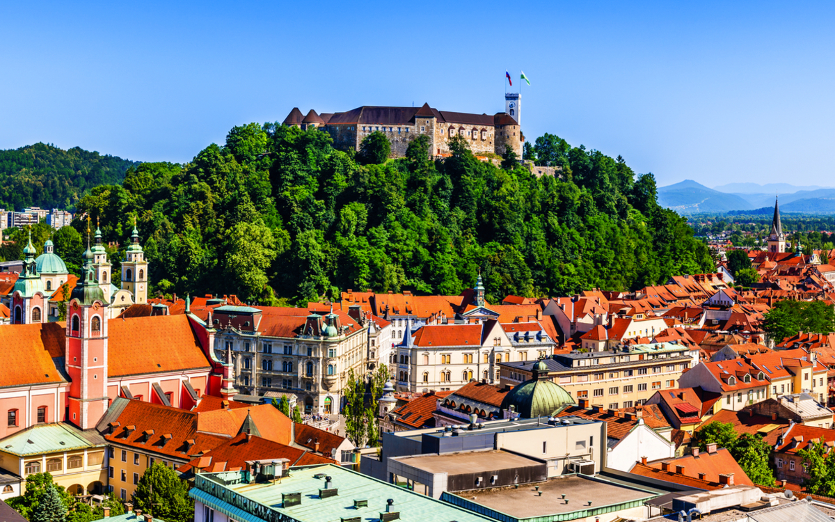 Panorama von Ljubljana mit Burg auf einem Hügel, umgeben von roten Dächern.