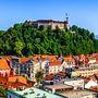 Panorama von Ljubljana mit Burg auf einem Hügel, umgeben von roten Dächern.