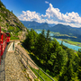 Rote Zahnradbahn fährt am Berg, Panorama mit See und Bergen im Hintergrund.