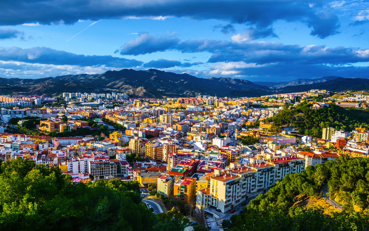 Blick auf eine Stadt mit bunten Gebäuden und Bergen im Hintergrund unter blauem Himmel.