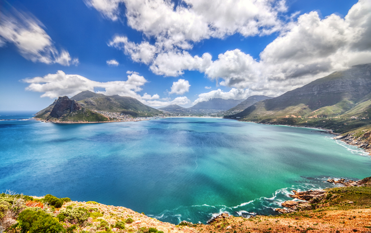 Panoramablick auf eine Bucht mit blauem Wasser und umgebenden Bergen.