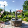 Brunnen im Park mit Mühle und blühenden Blumen im Hintergrund.
