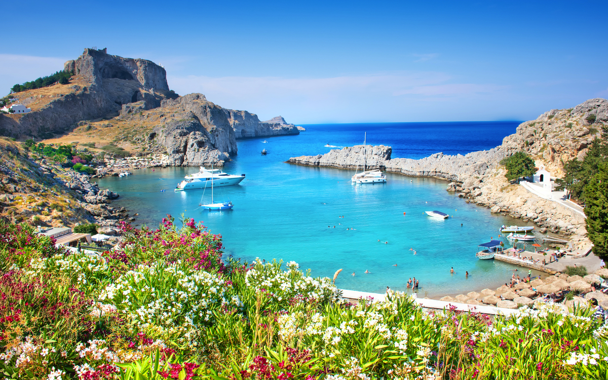Malerische Bucht mit blauem Wasser, Segelbooten und grünen Hügeln im Hintergrund.