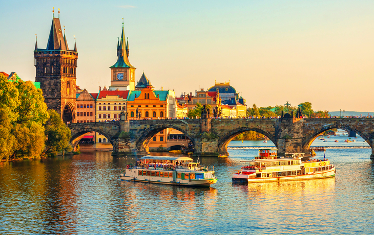 Boote auf einem Fluss vor einer alten Steinbrücke in einer Stadt bei Sonnenuntergang.