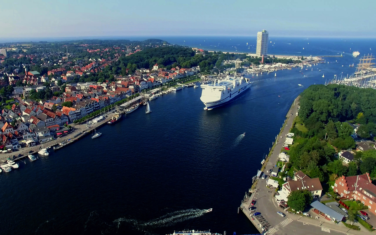 Luftaufnahme eines Hafens mit einem großen Kreuzfahrtschiff und Küstenstadt im Hintergrund