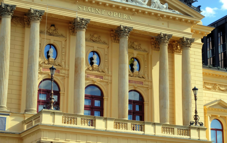 Fassade der Staatsoper Prag mit Säulen und Skulpturen bei Sonnenuntergang.