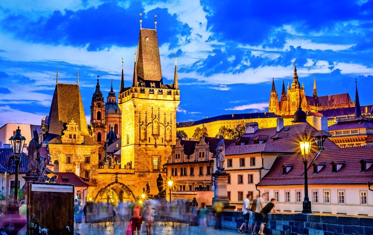 Karlsbrücke in Prag bei Sonnenuntergang mit Menschen und blauem Himmel.