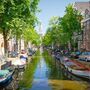 Blick auf eine typische Amsterdamer Gracht mit Booten, gesäumt von Bäumen und traditionellen niederländischen Gebäuden.