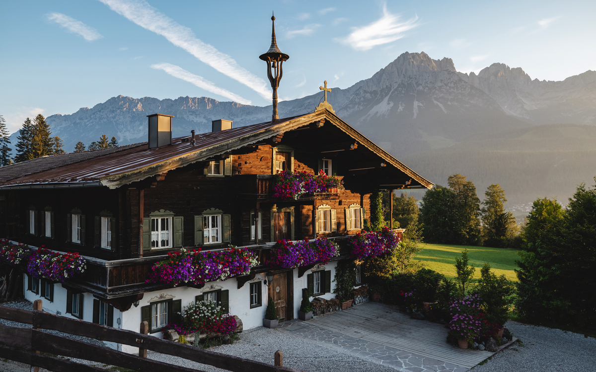 Traditionelles Holzhaus mit Blumen vor Bergkulisse bei Sonnenschein.