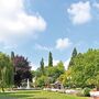 Ein Park mit grünen Bäumen, Springbrunnen und Sitzbänken unter blauem Himmel.