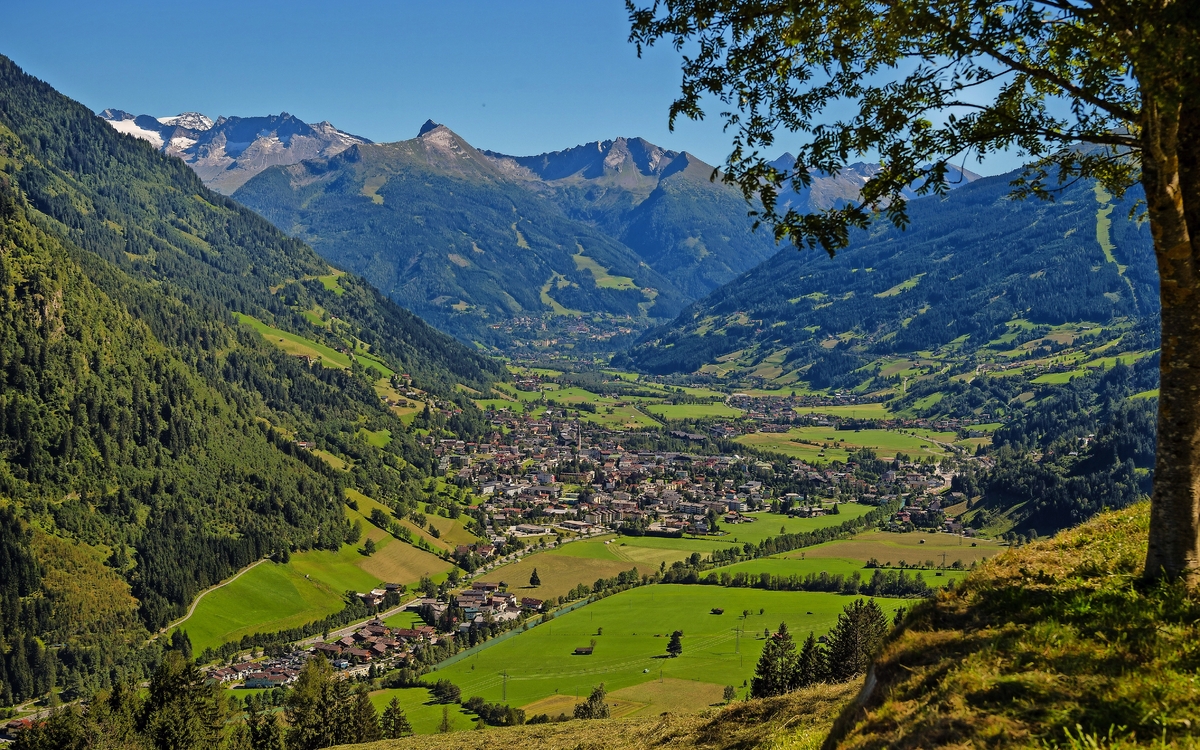 Blick auf ein grünes Tal mit einer Stadt, umgeben von Bergen und blauen Himmel.