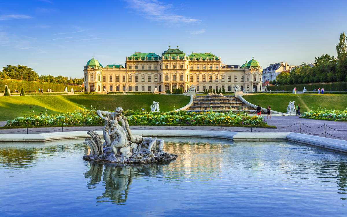 Barockschloss mit Garten und Teich im Vordergrund bei sonnigem Himmel.