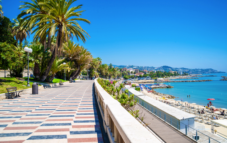 Strandpromenade mit Palmen und Blick auf das Meer bei sonnigem Wetter.