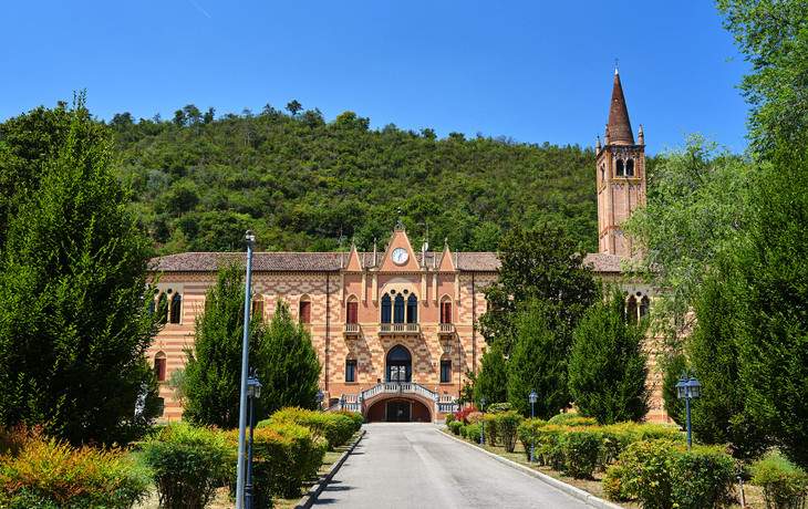 Historisches Hauses der Gastfreundschaft   mit Turm vor grünem Hügel unter blauem Himmel.
