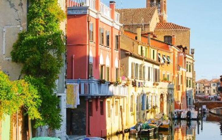 Bunte Häuser und Boote an einem sonnigen Kanal in Italien.