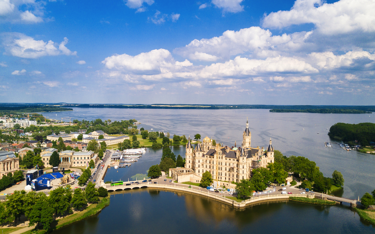 Luftaufnahme eines Schlosses am Wasser unter blauem Himmel und Wolken.