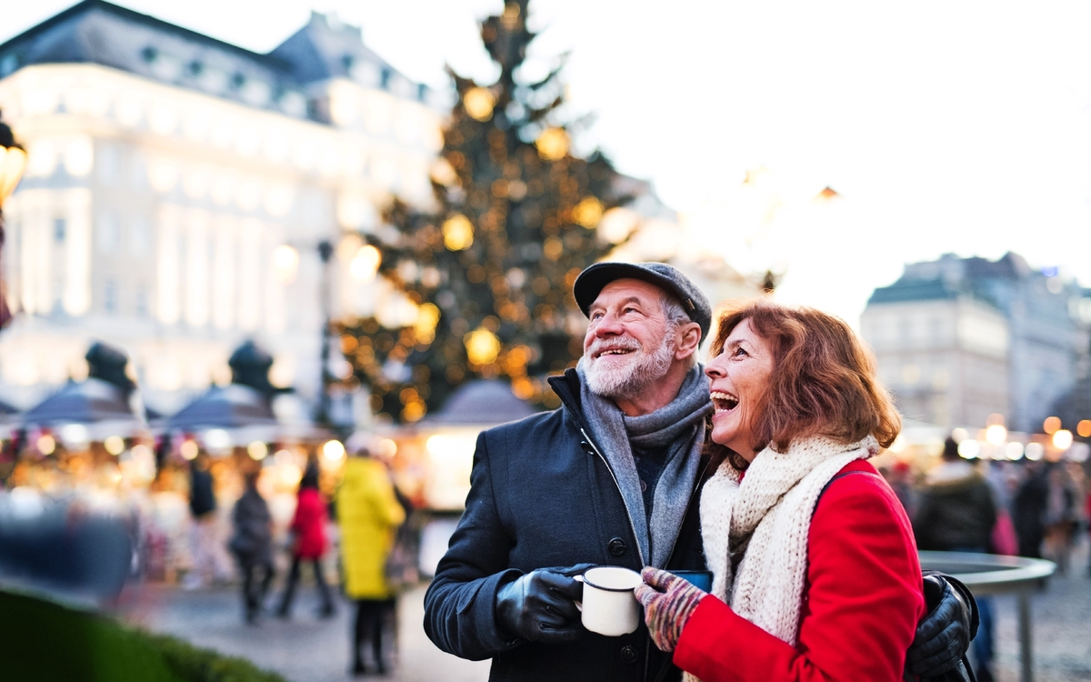 Älteres Paar auf einem Weihnachtsmarkt vor einem geschmückten Baum.