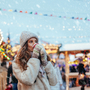 Frau mit Mütze und Handschuhen trinkt auf einem Weihnachtsmarkt im Schnee.