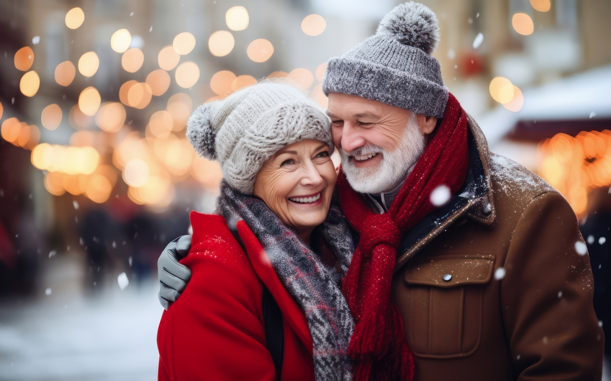 Älteres Paar lächelt im Winter bei Lichterkulisse draußen.