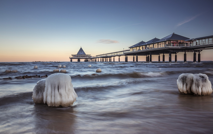 Vereister Steg am Meer bei Sonnenuntergang mit klarem Himmel im Hintergrund.