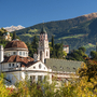 Kirchturm und Gebäude vor Alpenlandschaft im Herbstlicht