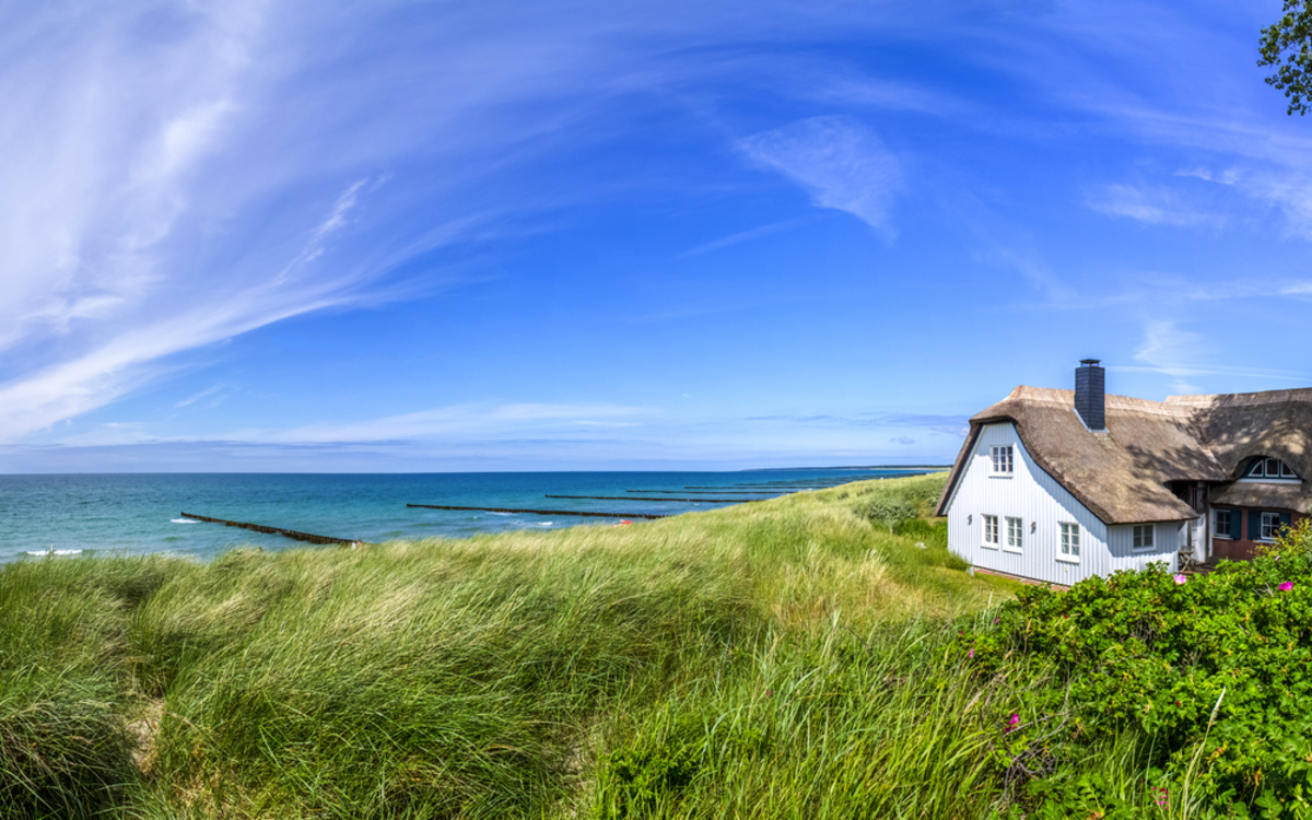 Reetdachhaus am Strand mit blauem Himmel und Dünenvegetation.