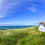 Reetdachhaus am Strand mit blauem Himmel und Dünenvegetation.