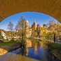 Blick von unter Brücke auf Fluss und Stadt im Sommer mit Türmen und Bäumen.