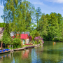Flusslandschaft mit Booten und Häusern, umgeben von grünen Bäumen.