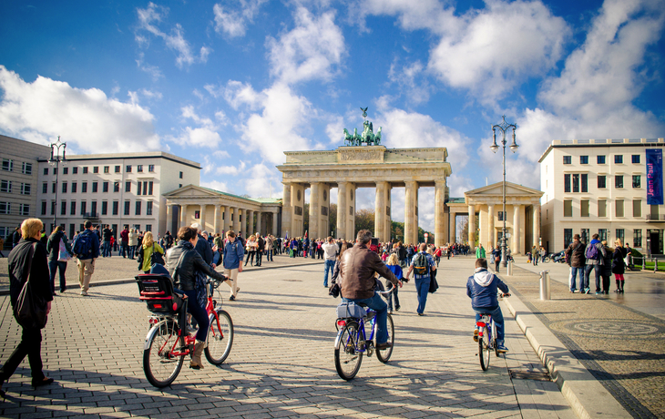 Menschen fahren mit Fahrrädern vor dem Brandenburger Tor in Berlin bei schönem Wetter.
