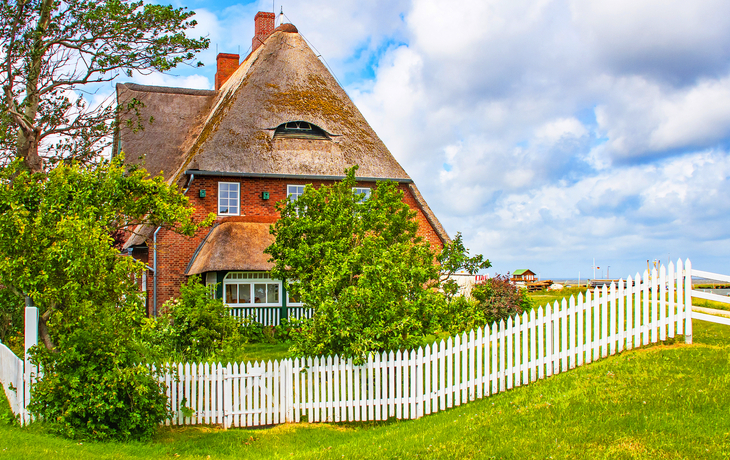 Reetdachhaus mit weißem Zaun und Garten im Hintergrund.