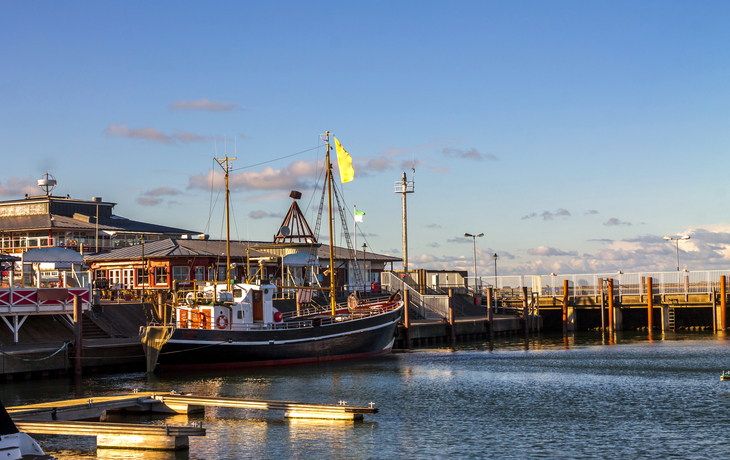 Hafen mit Booten und Gebäuden bei klarem Himmel und Sonnenschein.