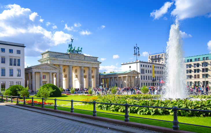 Brandenburger Tor in Berlin mit Springbrunnen und blauen Himmel.