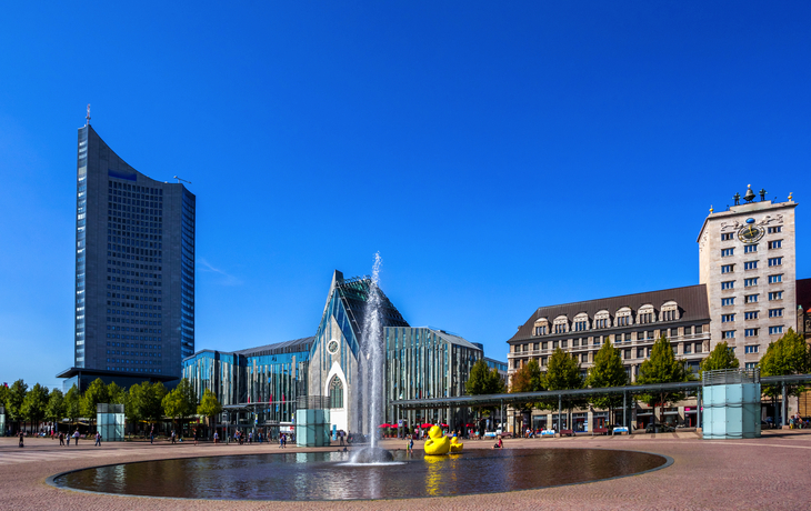 Springbrunnen und Gebäude am Augustusplatz in Leipzig bei klarem Himmel.