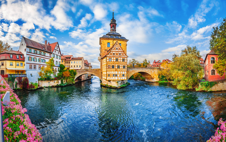 Historisches Fachwerk-Rathaus auf Brücke über Fluss in Bamberg, sonniger Tag.