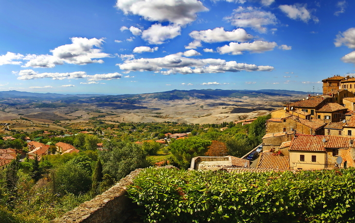 Ausblick auf eine italienische Hügellandschaft mit mittelalterlicher Stadt und blauem Himmel.