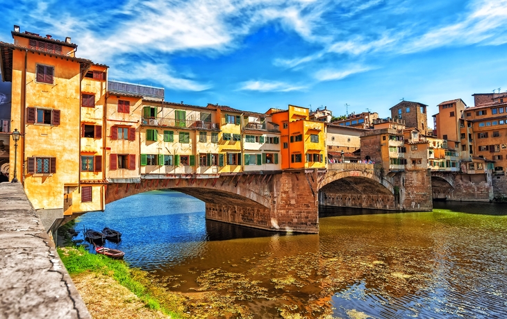 Historische Brücke mit bunten Gebäuden und Fluss unter blauem Himmel.