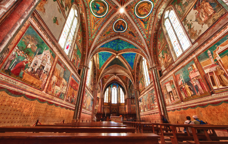 Innenansicht einer reich verzierten Kirche mit Fresken und Bänken.